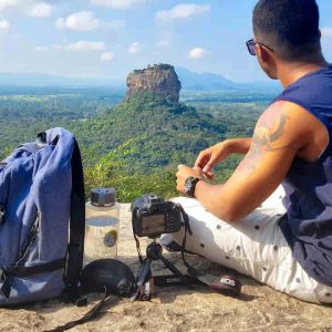 Man Sitting on Top of Gray Cliff Mountain Beside Backpack