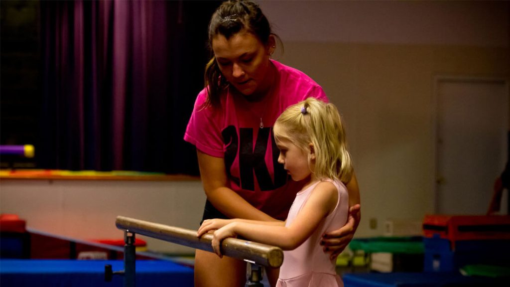 trainer teaching gymnastics to a young girl