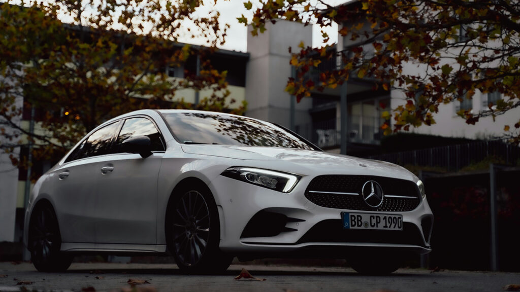a white luxury Mercedes-Benz A-Class is parked near the trees