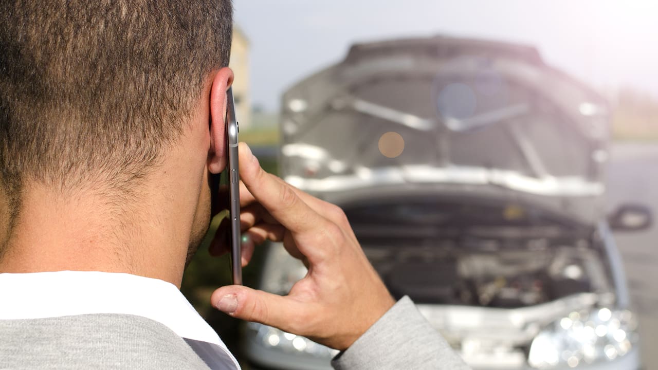 A man stands by his broken vehicle and making a phone call 