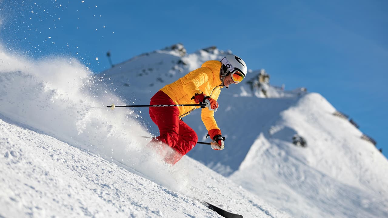 A person wearing a yellow jacket is skiing on a snowy mountain, which is an extreme sport