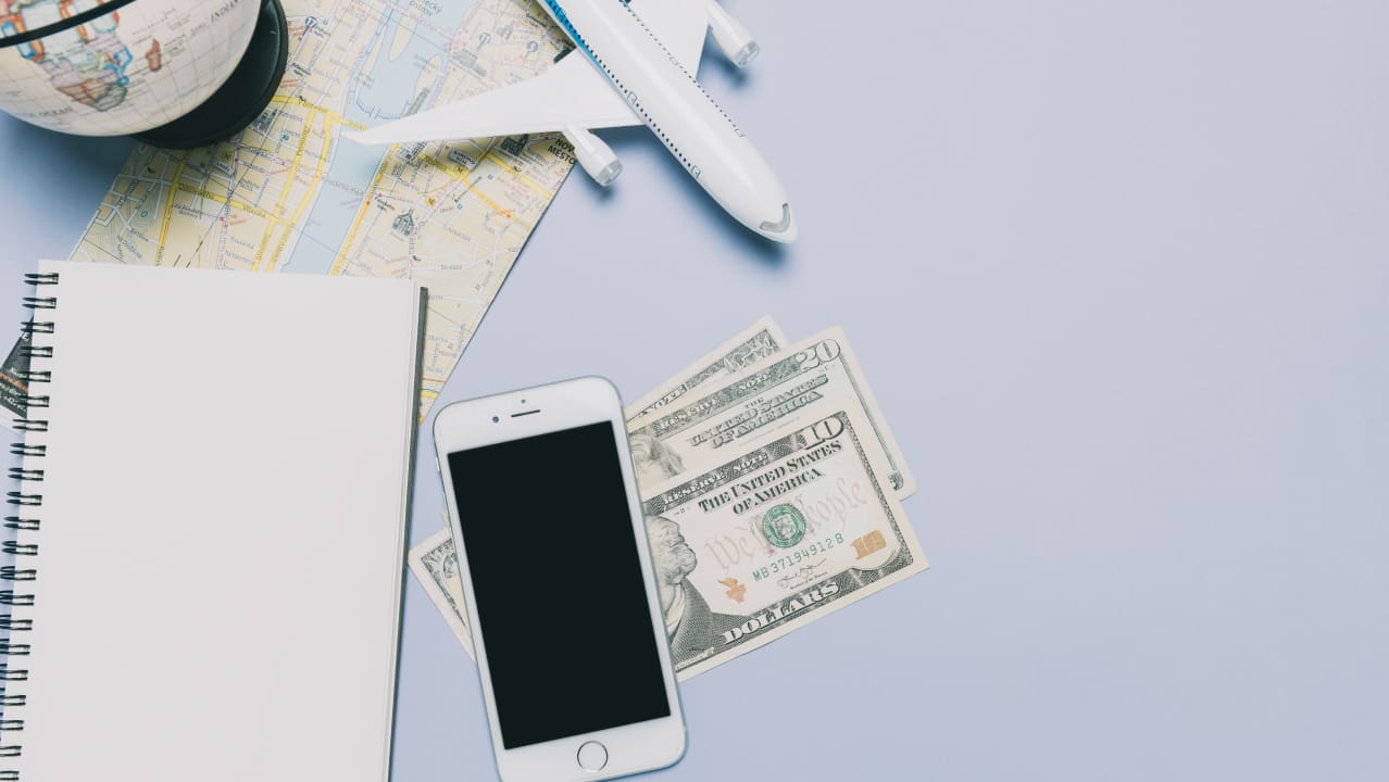 A table that has a phone, some money, and a notebook on it