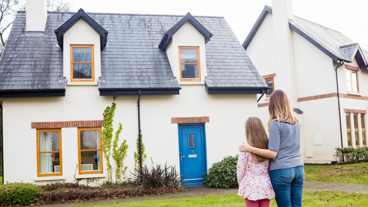 A mother and daughter are standing together, looking at the house