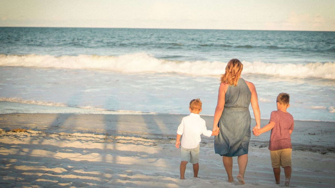 A mother holding hands of his two sons on a beach shore