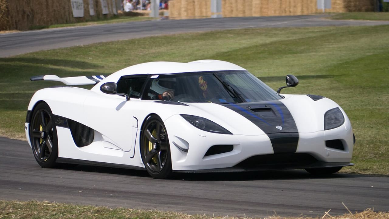 A man is driving a white Koenigsegg along the roadside