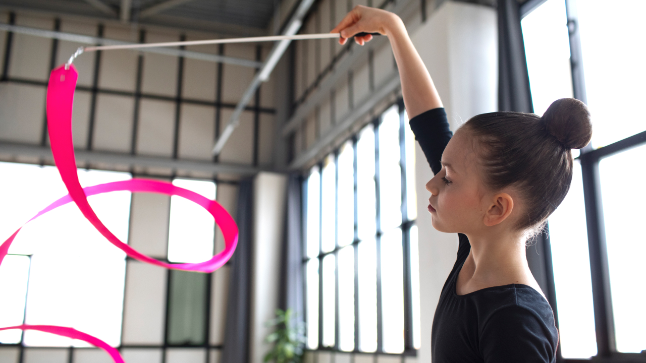 A young girl playing with a stick while practicing for gymnastics