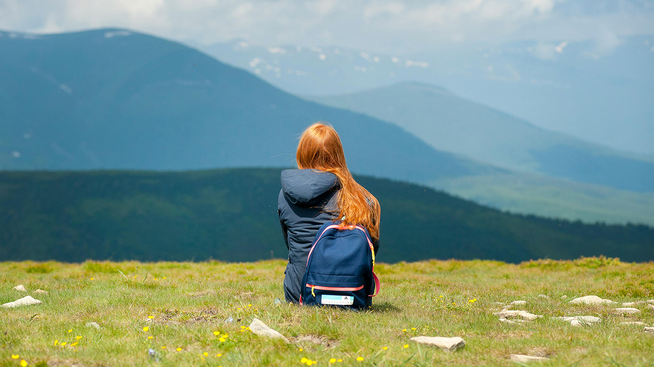 A girl wearing gray jacket and sitting on grassy field