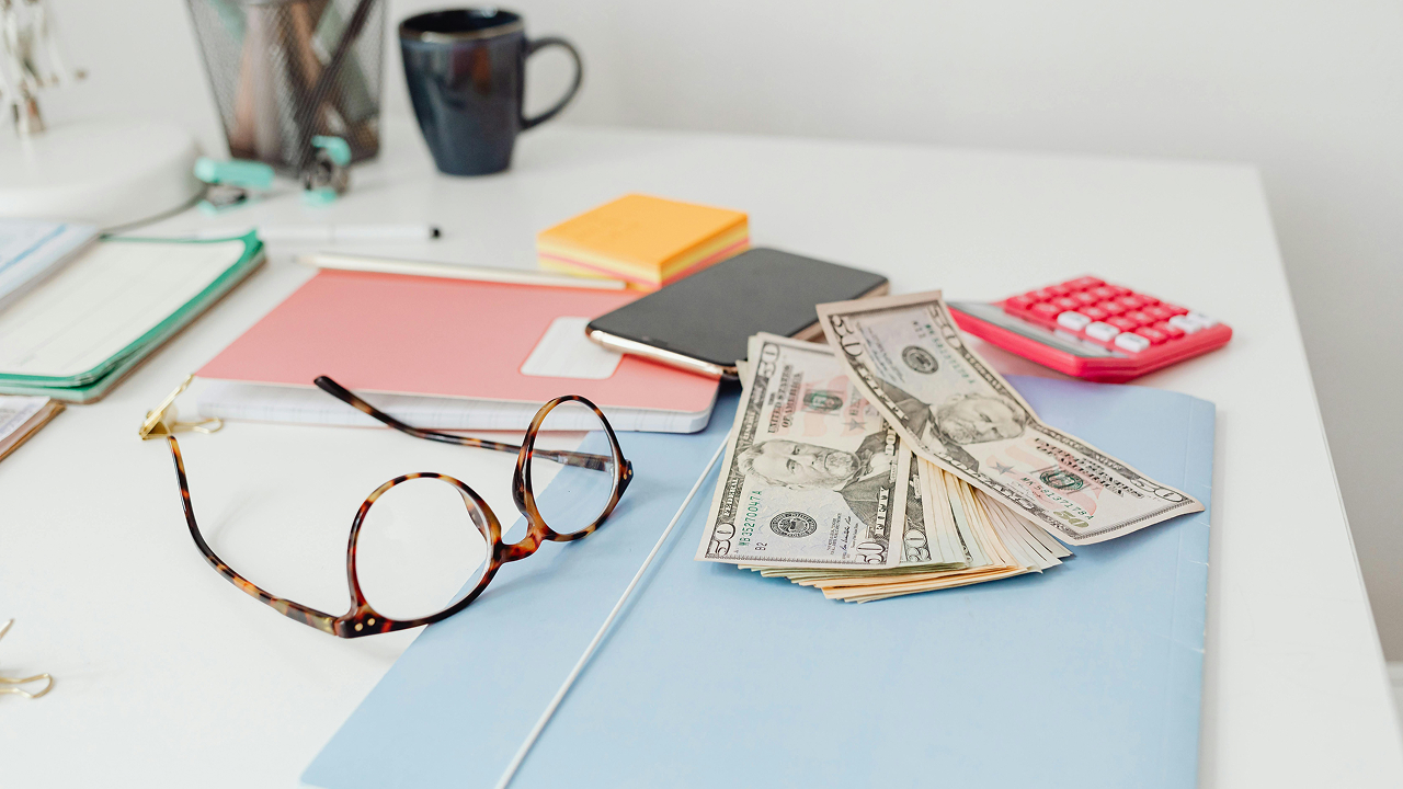 A close-up shot of a table with a pair of eyeglasses and some cash on it
