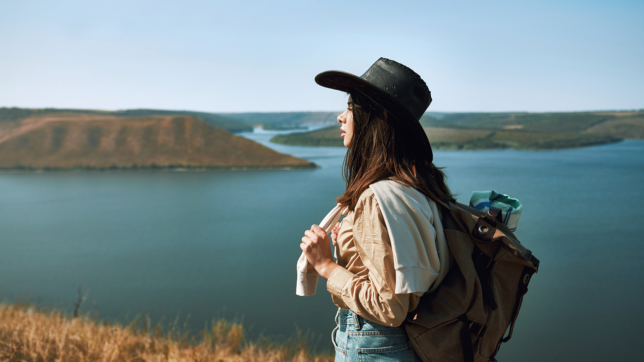 Side pose of a woman wearing a hat and a backpack going for a solo travel