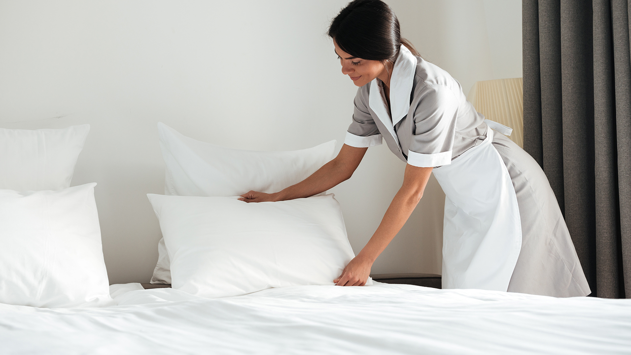 A girl setting up a pillow on a bed.