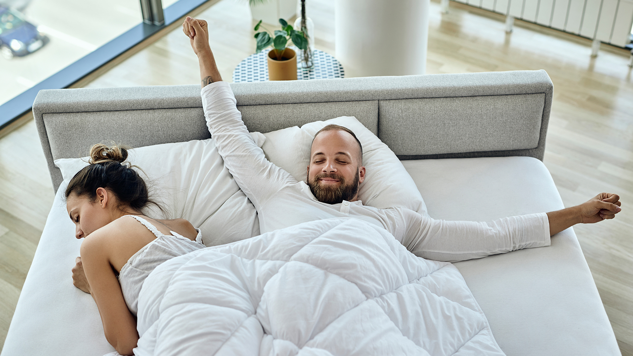 A man and his wife stretching comfortably in bed on mattress toppers