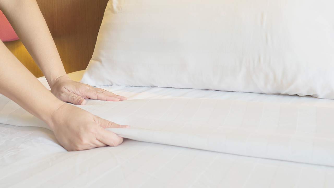 A woman placed her hands on a mattress topper spreading the sheet