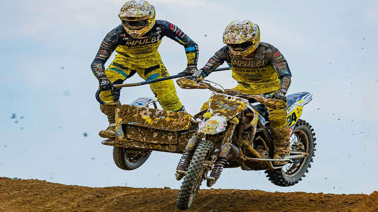 racers are performing aerial stunt with one man standing on the side car in sidecarcross