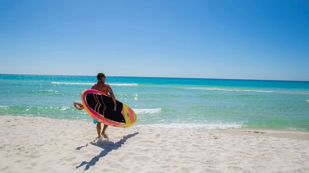 A man carrying a water skate is walking towards the beach